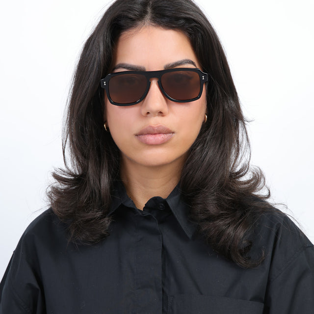 Brunette model with loose curls wearing Trancoso Sunglasses Black with Brown