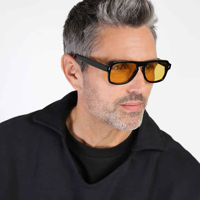 Model with salt and pepper hair and beard looking left wearing Trancoso Sunglasses Black with Honey See Through