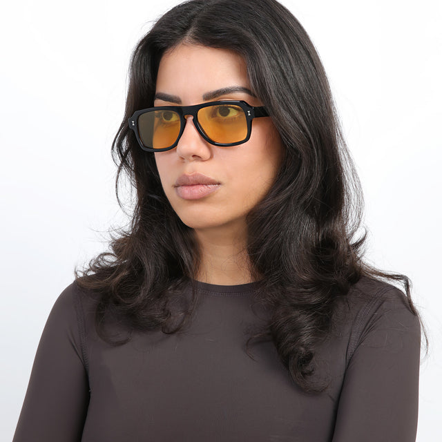 Brunette model with loose curls looking right wearing Trancoso Sunglasses Black with Honey See Through