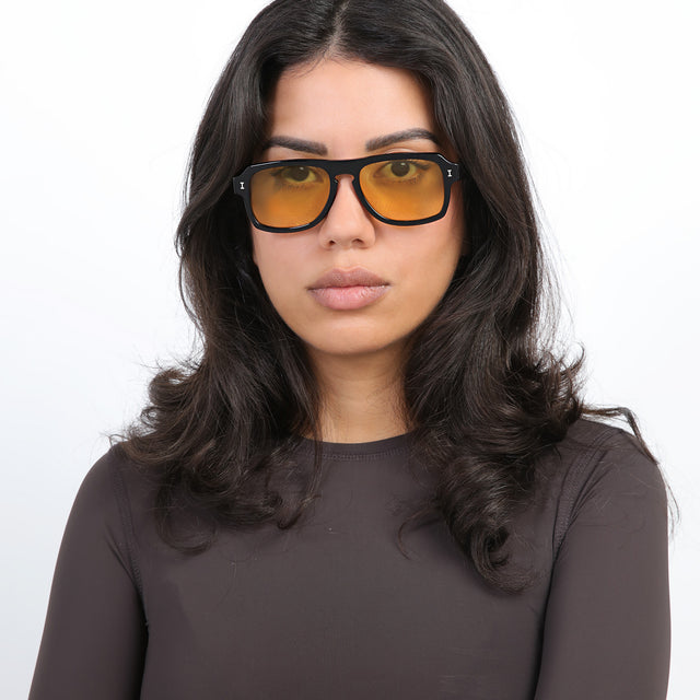 Brunette model with loose curls wearing Trancoso Sunglasses Black with Honey See Through