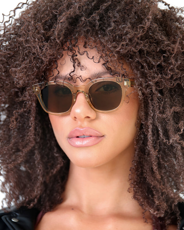 Brunette model with afro-curly hair wearing Vail Sunglasses Citrine with Brown Flat