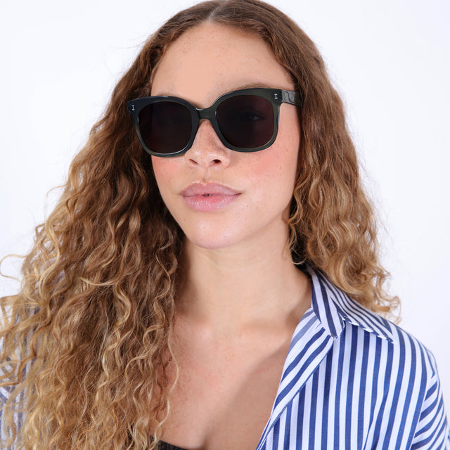 Brunette model with ombré, natural curls wearing Valencia Sunglasses Pine with Grey