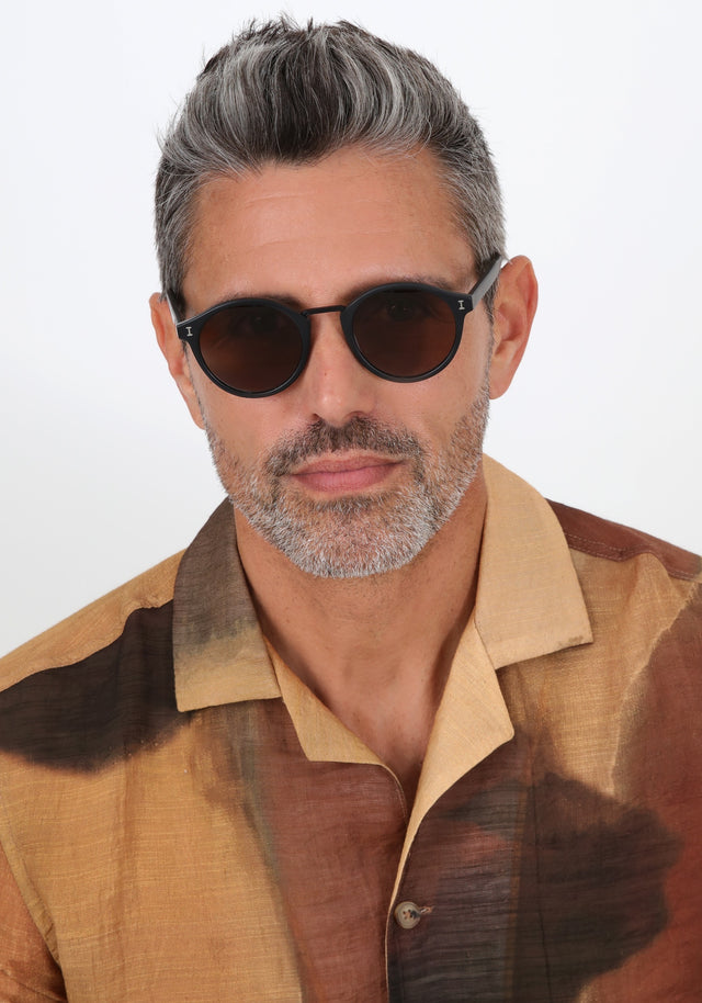 Model with salt and pepper hair and beard wearing Village Sunglasses in Matte Black