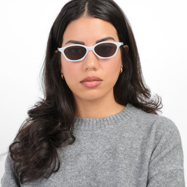 Brunette model with loose curls wearing Vilma Sunglasses Light Grey