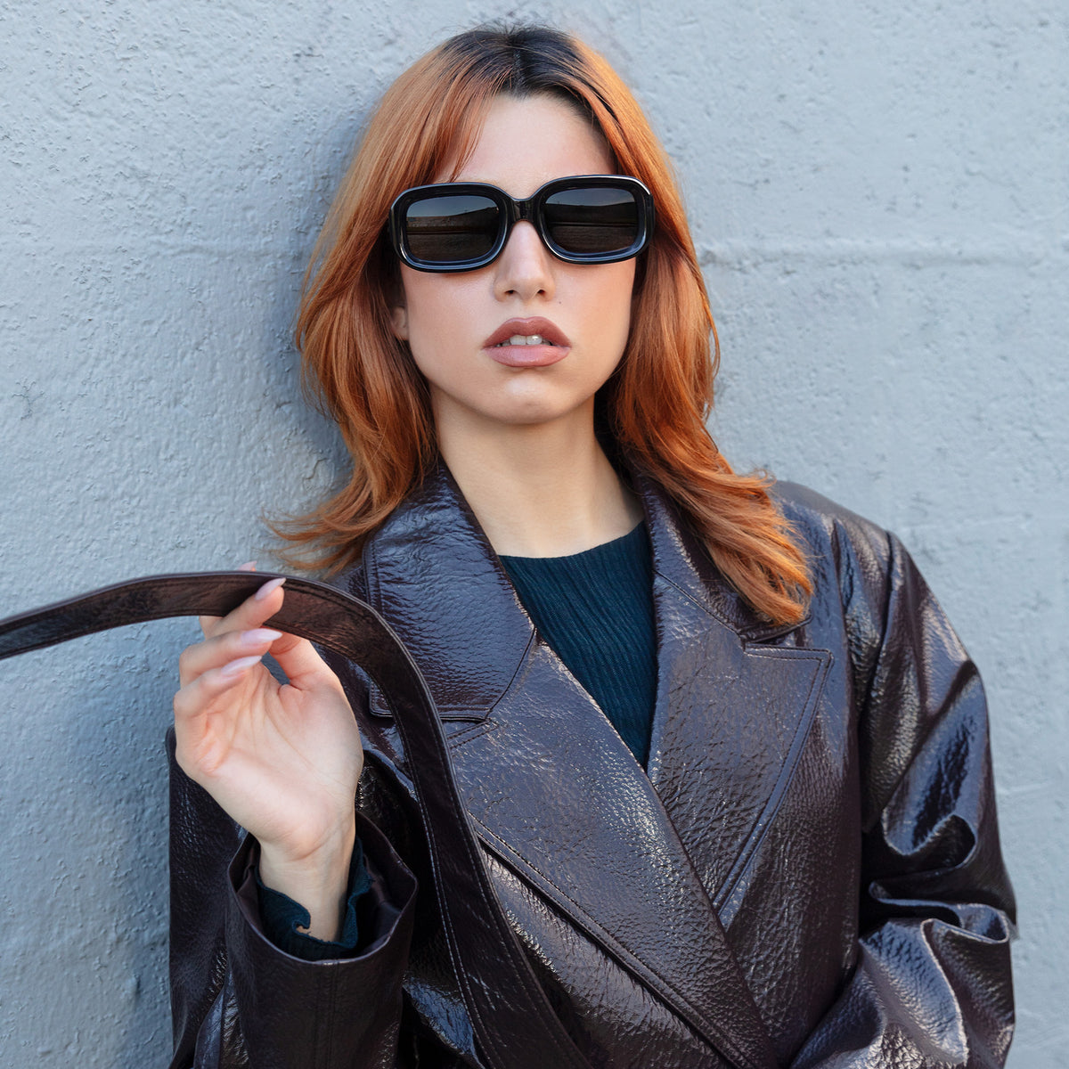 Woman wearing Vinyl Sunglasses in Black with Grey lenses, Model in a leather jacket holding her leather belt