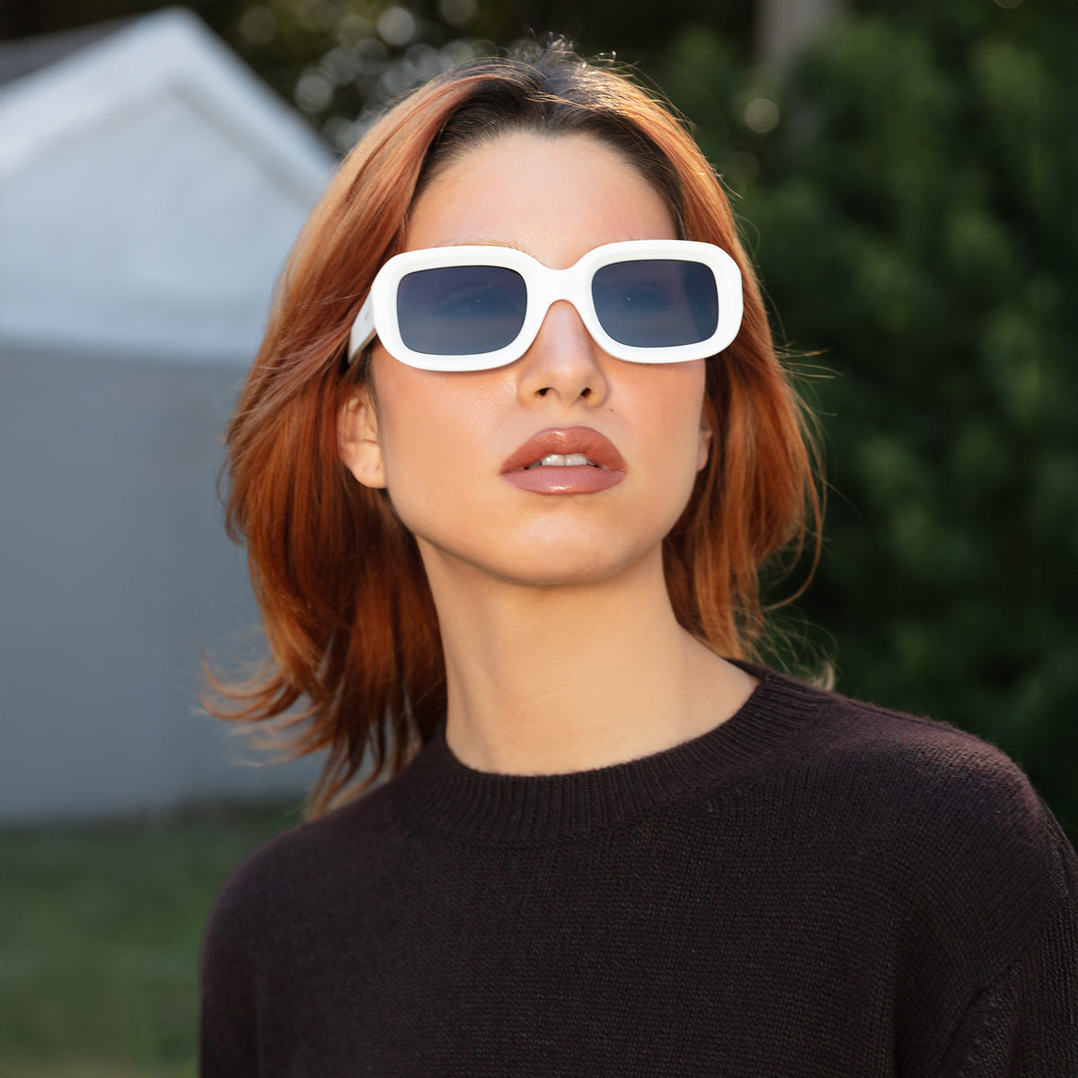 Woman wearing Vinyl Sunglasses in White with Grey lenses, Model outside a cabin