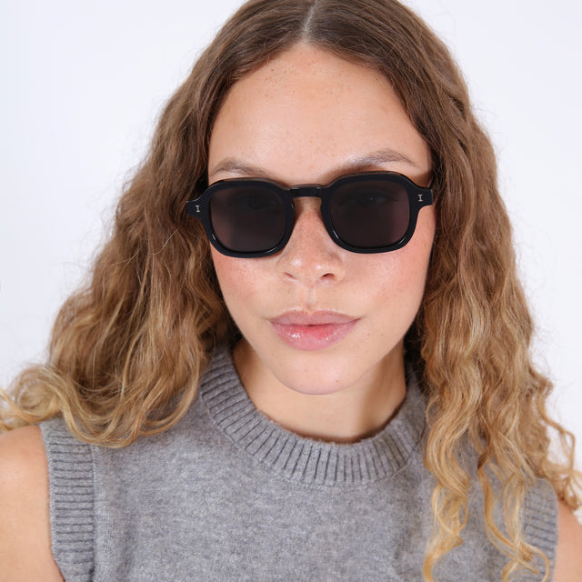 Brunette model with wavy hair in a grey mockneck wearing Washington Sunglasses Black with Grey Flat