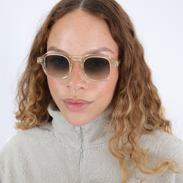 Brunette model with wavy hair in a cream fuzzy jacket wearing Washington Sunglasses Champagne with Olive Flat Gradient
