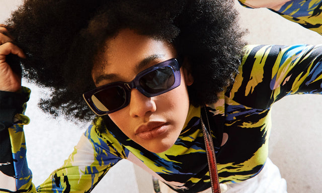 Model with afro curly hair wearing nk x illesteva Wilson Sunglasses Cobalt/Black with Grey Flat