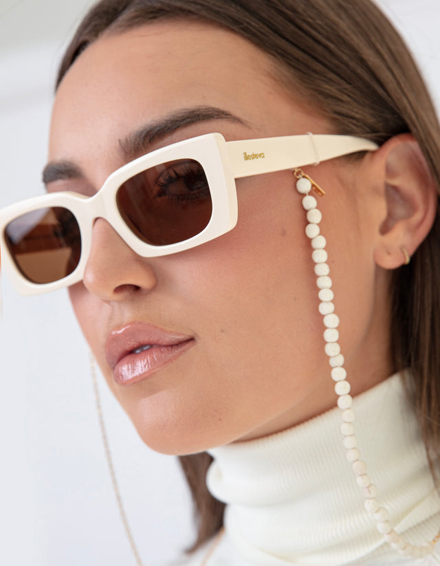 Brunette model in a white turtleneck wearing Wilson Sunglasses in Cream with Brown lenses and a sunglass chain
