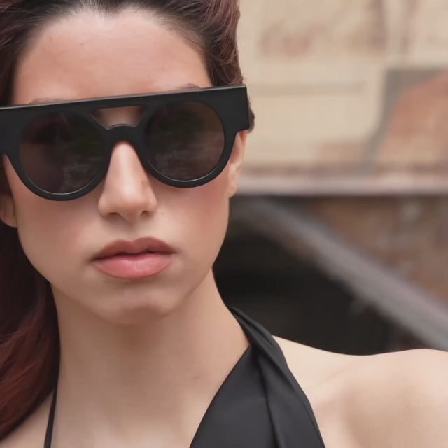 Woman with red hair wearing the Meyer 15 Year Anniversary Sunglasses in Matte Black near a train passing by