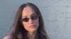 Woman wearing the Marianne sunglasses in Grey near a painted brick wall