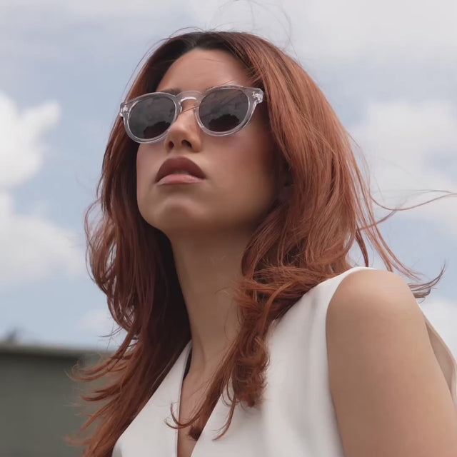 Woman with red hair wearing the Leonard 15 Year Anniversary Sunglasses in Clear/Havana near a train passing by