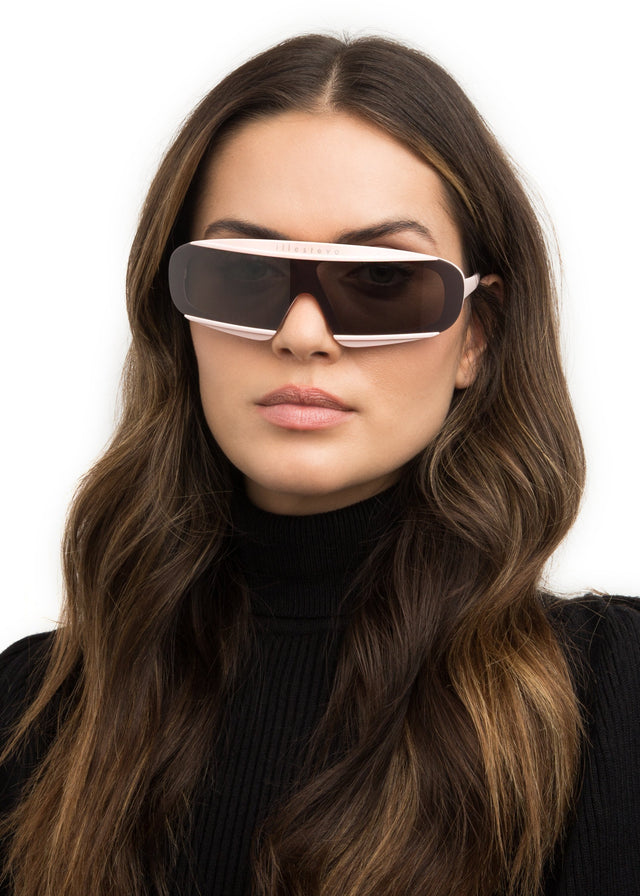 Brunette model with wavy curls wearing Courchevel Sunglasses Matte Blush with Grey