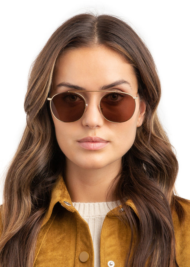 Brunette model in a gold velvet jacket wearing Mykonos II Sunglasses Gold with Brown Flat